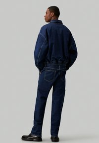 Denim jakna in hlače v temno modri barvi. Jakna ima ovratnik in elastiko v pasu. Hlače imajo pet žepov in ravno obliko nogavic.