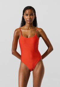 Rød badedragt i ét stykke med tynde stropper, en rund halsudskæring og sømløst design. Har en subtil glans og minimal hardware-detalje.