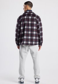 Ruudullinen flanellipaita tummanpunaisena, merimiehen sinisenä ja valkoisena; rento leikkaus pitkillä hihoilla. Yhdistetty vaaleanharmaisiin collegehousuihin ja valkoisiin lenkkareihin.