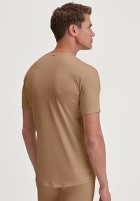 Lichtbruine, korte mouwen, getailleerde shirt gemaakt van soepel materiaal; heeft een ronde halslijn en een detail in de achternaad.
