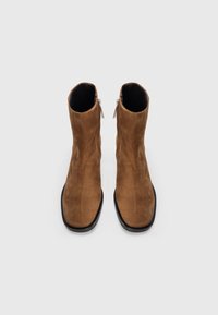Stivaletti in suede marrone con una texture liscia, punta quadrata e cerniere laterali, caratterizzati da un rivestimento interno nero e suole nere eleganti.