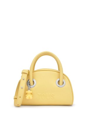 Bolso de cuero amarillo con asas redondeadas, ojales plateados, logo "TOUS" en relieve y un pequeño colgante de osito adjunto a una de las asas.