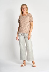 Helles beiges Kurzarmoberteil mit Zebra-Streifen, kombiniert mit hellen Denim-Weitbein-Hosen und beigen Slip-On-Sandalen. Einfaches Design und entspannte Passform.