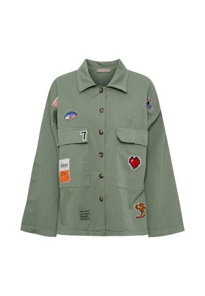Olivengrøn jakke med knapper, brede ærmer, forlommer med klap og forskellige farverige patches, herunder et hjerte, tallet 7 og tegneseriefigurer.