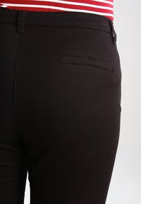 Černé kalhoty slim fit, s jednou zadní kapsou, poutky na pás a hladkým povrchem. Pas je mírně elastický.