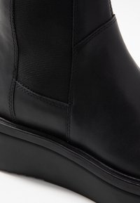 Black leather ankle boot featuring a smooth texture, elastic side panel, and a sturdy black rubber sole with a slight wedge.