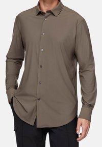 Camicia marrone a maniche lunghe con chiusura a bottoni, texture liscia, colletto a punta e orlo arrotondato; presenta bottoni neri per la chiusura.