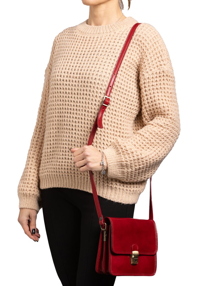 Borsa a tracolla rossa in pelle con hardware dorato, dotata di chiusura a patta e cuciture a contrasto, tenuta da una persona in un maglione beige texturizzato.