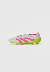 Botas de fútbol con parte superior blanca, detalles en rosa y azul, y una suela verde brillante. Presentan un diseño texturizado y ojales visibles.