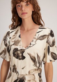 Blumenkleid mit V-Ausschnitt, kurzen schwingenden Ärmeln, cremefarbener Basis und dunklem schwarz-braunem botanischen Druck, mit einer taillierten Taille.