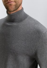 Grijze coltrui van fijn gebreide stof, met een geribde kraag en subtiele logo-detail op de borst.