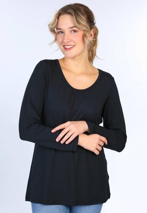 Schwarzes Langarmoberteil mit weiter Ausschnitt und Raffung in der Mitte. Aus einem glatten Stoff gefertigt, kombiniert mit hellblauen Jeans.