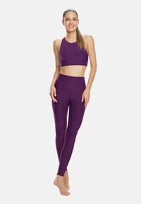 Lila sportmelltartó és magas derekú leggings, mindkettő sima, rugalmas anyagból készült. A dizájn szoros, kiemeli a test vonalait.