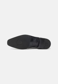 Suola di una scarpa elegante in pelle nera con logo impresso e dettagli di cucitura su uno sfondo bianco.