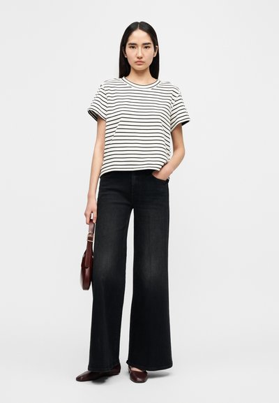 Ριγέ κοντομάνικη μπλούζα σε μαύρο και λευκό, συνδυασμένη με μαύρο τζιν παντελόνι ψηλόμεσο και φαρδύ. Το μοντέλο κρατά μια μικρή καφέ τσάντα.