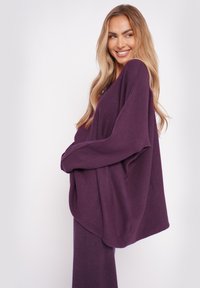 Lockere lila Strickjacke mit langen Ärmeln und weiter Passform, die eine weiche Textur und eine drapierte Silhouette aufweist.