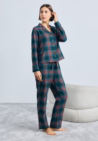 Modrý a zelený kockovaný pyžamový set so zapínaním na gombíky a elastickým pásom na nohaviciach. Materiál vyzerá mäkký; má dlhé rukávy a klasický golier.
