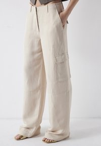Beżowe szerokie spodnie cargo z bocznymi kieszeniami, wykonane z lekkiego materiału, z płaskim przodem i subtelnymi detalami szycia.