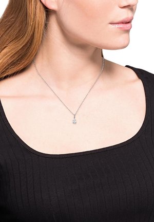 Collana d'argento con una delicata catena, caratterizzata da un pendente a forma di goccia decorato con un cristallo trasparente, indossata sopra un top scuro.