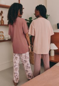 Dwie modelki noszące luźne bluzki; jedna w kolorze fiołkowym, druga w jasnoróżowym. Do tego wzorzyste i w paski spodnie do spania. Teksturowane tła.