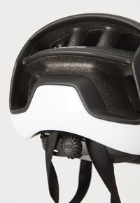 Fahrradhelm mit einer weißen Außenschale, schwarzen Akzenten, Belüftungsöffnungen, strukturiertem Innenraum und einem verstellbaren Dial für die Passform.