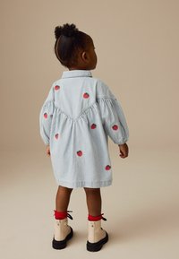 Gestreiftes Baumwollkleid mit bestickten roten Erdbeeren, Puffärmeln und gerafftem Rücken. Kombiniert mit beigen Stiefeln und roten Knö socks.