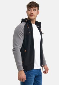Sudadera con cremallera en negro y gris, con cordón y detalles en cuero, además de bolsillos tipo canguro. Material de mezcla de algodón, diseño ajustado.