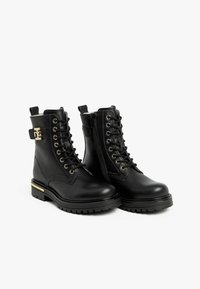 Bottines en cuir noir à lacets et fermeture éclair, avec des accents de quincaillerie dorée et une semelle texturée. Design chunky avec une finition lisse.