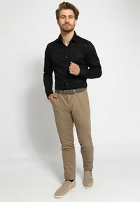 Zwart overhemd met lange mouwen, beige broek en beige instapschoenen. Het overhemd heeft een knoopsluiting; de broek is slim-fit en heeft een textuur.