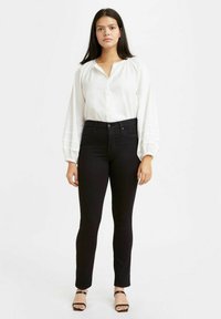 Blusa blanca de manga larga con cierre de botones y jeans ajustados negros. La modelo lleva sandalias de tacón negras. Tela sencilla y suave sin patrones.