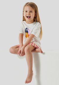 T-shirt blanche avec un imprimé abstrait coloré, associée à un short rayé. Le matériau semble doux ; la coupe est décontractée.