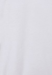 Tissu en coton blanc avec une surface douce et légèrement texturée ; présente une apparence lisse, adaptée pour un port décontracté ou en superposition.