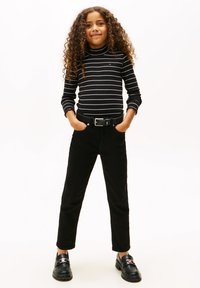 Sort og hvidstribet langærmet turtleneck, sort bælte, sorte bukser og sorte loafers med en sølvspænde. Krøllet hår.