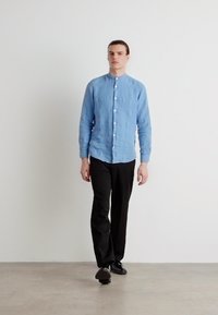 Lichtblauwe langarmige button-up shirt van een textuur stof, gecombineerd met zwarte broek en zwarte schoenen, tegen een witte achtergrond.