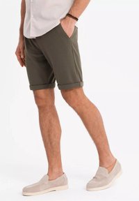 Olivgröna shorts med upplagda muddar, tillverkade av texturerat tyg, med sidofickor. Kombinerat med ljusbeige slip-on skor.