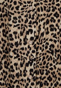 Tela beige con patrón de estampado de leopardo negro y tres botones redondos visibles, similares a perlas, dispuestos en fila vertical.