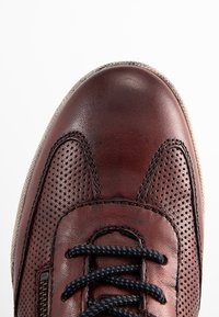 Sneaker in pelle marrone con design perforato, punta rotonda, lacci scuri e suola chiara a contrasto. Finitura liscia e texture.