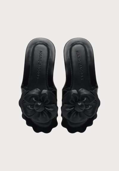 Paire de sandales noires à enfiler avec de grandes décorations florales à l'avant et des bords festonnés, vue de dessus. Nom de la marque visible sur les semelles intérieures.
