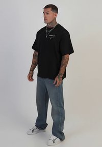 Musta ylipitkä t-paita, jossa edessä logo, vaaleansiniset farkut ja valkoiset lenkkarit. Mukana tatuointeja ja kerroksittain hopeisia kaulakoruja.