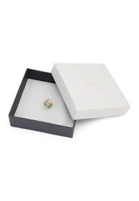 Goldfarbener Ring mit drei gestapelten Bändern, versehen mit dezenten Steinelementen, präsentiert in einer gepolsterten schwarzen Box mit einem weißen strukturierten Deckel.