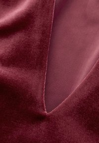 Tissu en velours bordeaux à texture lisse, présentant une coupe en V profonde et une doublure côtelée contrastante dans une teinte marron clair.