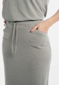 Lichtgrijze gebreide rok met een elastische tailleband, een trekkoord en zijzakken. De stof lijkt zacht met een gladde textuur.