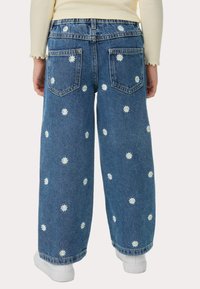 Jeans de denim de pierna ancha con bordado de margaritas en blanco y amarillo. Cuenta con cinco bolsillos y una cinturilla regular. Tejido azul claro con un acabado texturizado.