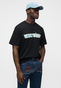 Μαύρο βαμβακερό κοντομάνικο με γραφικό "παγωτό" σε μπλε και κίτρινο. Συνδυάζεται με σκούρο τζιν με πολύχρωμα στρας στα τσέπες.