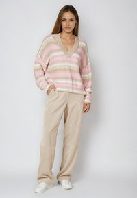 Striped sweater in pastel pink and beige with a V-neck and dropped shoulders, paired with beige corduroy wide-leg pants and white sneakers.