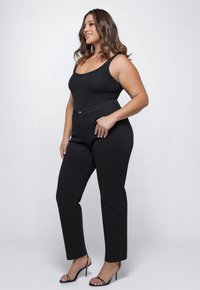 Zwarte geribbelde tanktop gecombineerd met hooggepolsterde zwarte jeans. Model draagt zwarte strappy hakken, met een focus op eenvoudige en elegante ontwerpelementen.