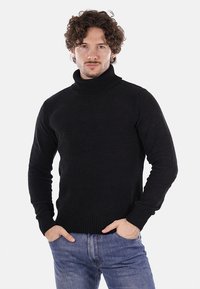 Maglione nero a collo alto caratterizzato da una texture a coste, maniche lunghe e un design aderente, indossato con jeans blu.
