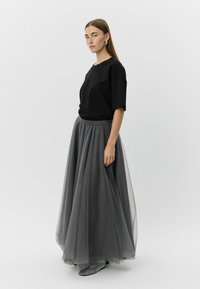 Must have musta T-särk lühikeste varrukatega on kombineeritud põrandapikkuse, läbipaistva halli tüllseelikuga. Musta ja valge mustriga kingad lõpetavad välimuse.