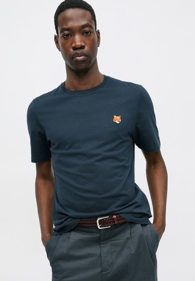 Tricou din bumbac de culoare bleu marin, cu mânecă scurtă, având un mic logo brodat al unei fețe de vulpe pe pieptul stâng. Textură netedă, design cu gât rotund.