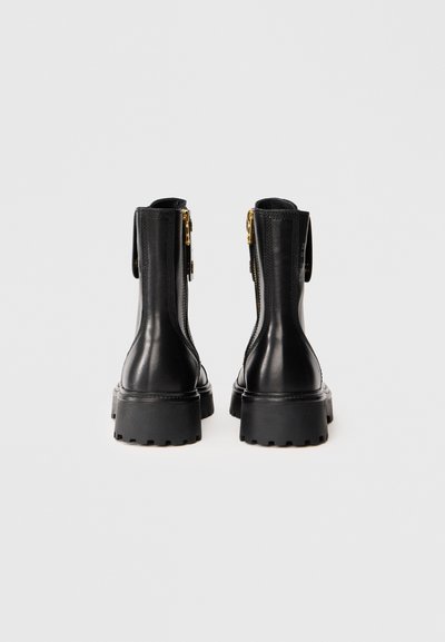 Black leather ankle boots with a textured finish, side zippers, lug sole, and gold hardware accents, viewed from the back.